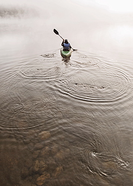 Young woman enjoys early morning paddle in kayak through mist on Daicey Pond in Maine's Baxter State Park, USA