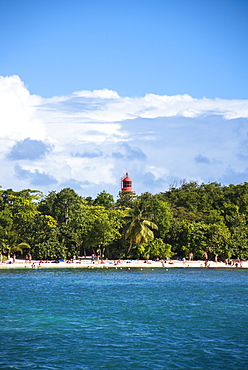 Scenic view of tourists on beach and lighthouse behind palm trees, Gosier, Guadeloupe