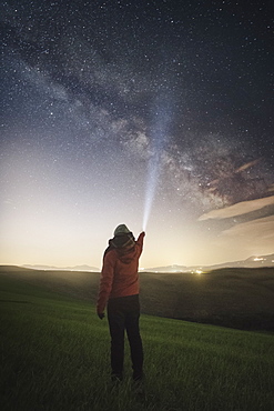 Milky Way galaxy and stars in sky above man shining flashlight at sky at dusk