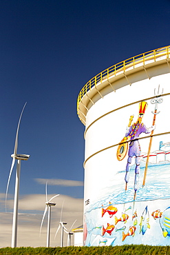 Climate change heaven and hell, an oil terminal in Amsterdam, Netherlands, with wind turbines generating renewable energy. Also a great example of green washing with happy fish depicted swimming round an oil tanker.