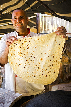 Happy Chef holding up freshly cooked, handmadeÂ shrakÂ (markook)Â Bedouin bread, Wadi Rum Village, Aqaba Governorate, Jordan