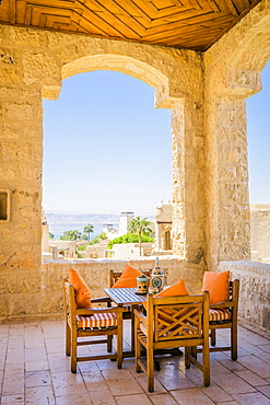 Table and chairs on covered terrace of Movenpick Dead Sea Spa and Resort with village in background, Madaba Governorate, Jordan