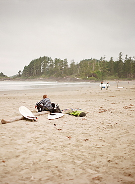 Surfer sitting on log on sandy beach, Vancouver, British Columbia, Canada