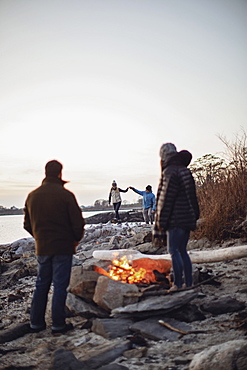 Group of friends enjoying time aroundÂ beachsideÂ campfire along coast, Peaks Island, Maine, USA