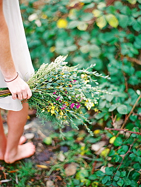 Low section shot of barefoot woman in white dress holding flowers