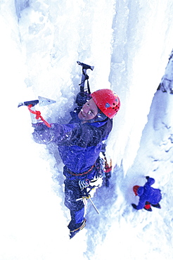 Eric Sast climbing an icy cliff with axes.