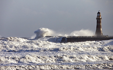 Waves Crashing Against A Pier With A Lighthouse