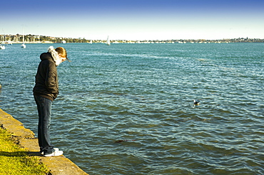 A Woman Standing On The Retaining Wall At The Water's Edge, Auckland, New Zealand