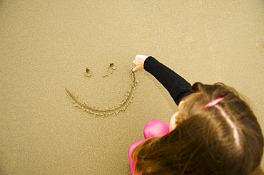 A Girl Draws A Happy Face In The Sand