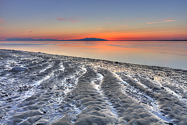 Ripples and patterns in the sand at the waters edge with a pink sunset on the horizon