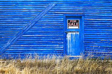 A blue barn with a for sale sign in the window of the door, Saskatchewan canada