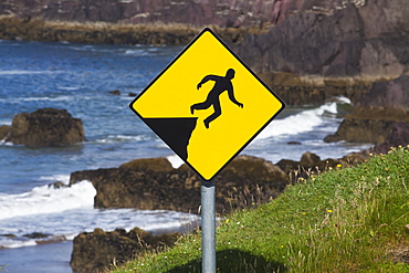 A yellow warning sign depicting a person falling off a cliff, County kerry, ireland