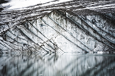 Layers in gravelly glacier cliff reflected in a small glacial lake, jasper national park, Alberta, canada