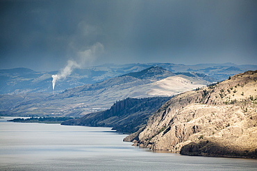 The dry hills of kamloops with a smokestack spewing pollution in the distance, Kamloops, british columbia, canada