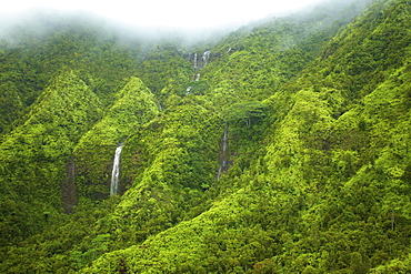 Waterfalls flowing through lush green hills under the low lying clouds, Hawaii united states of america