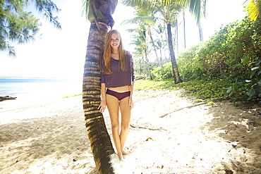 A young woman poses beside a palm tree on a beach, Kauai hawaii united states of america