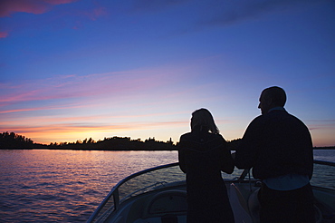 Middle aged couple travelling by motorboat in the lake of the woods at sunset, kenora ontario canada