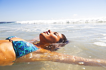 A young woman lays in the shallow water off the beach, Gold coast queensland australia