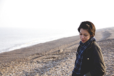 A Young Woman Stands On The Rocky Beach At The Water's Edge, Aldeburgh, England