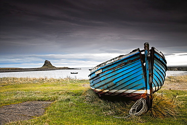 A Weathered Boat Sitting On The Shore With Lindisfarne Castle In The Distance, Lindisfarne, Northumberland, England