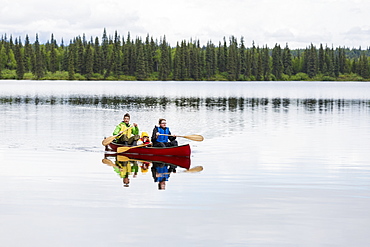 Family In Red Canoe On Byers Lake With Green Tree Covered Shoreline, Denali State Park, Alaska, Alaska, United States Of America