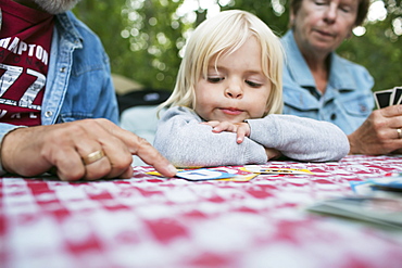 Grandparents Teaching A Young Granddaughter How To Play A Card Game, Peachland, British Columbia, Canada