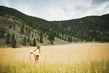 Two Young Girls Walking In The Tall Grass Of A Field, Peachland, British Columbia, Canada