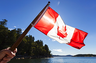 A Man Holds A Canadian Flag Into The Sun With The Gulf Islands The Distance, British Columbia, Canada