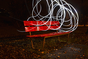 A Red Park Bench In Autumn With Swirls Of White Light In The Sky Around It, Locarno, Ticino, Switzerland