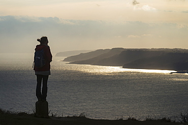 Silhouette Of A Woman Admiring The View Towards Lyme Regis From The Top Of Golden Cap On The Jurassic Coast, Seatown, Dorset, England