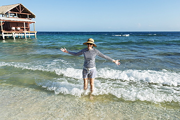 A Woman Stands In The Waves Beside A Hotel On The Coast, Utila, Bay Islands, Honduras