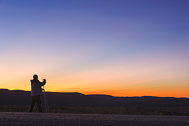 A Photographer Is Silhoutted Against The Sunset Above Eagle Summit Along The Steese Highway, Fairbanks, Alaska, United States Of America