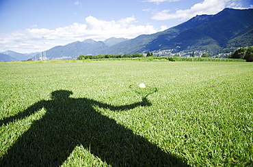 Shadow of a person holding a racquet being cast onto a ball sitting on the grass, Locarno ticino switzerland