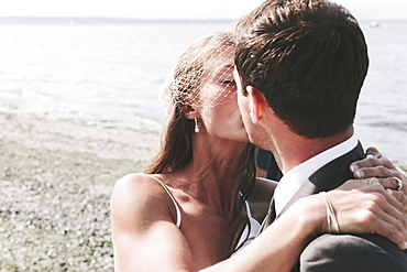 A bride and groom kissing on a beach at the water's edge, Kirkland washington united states of america