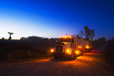 Agriculture - A grain truck at a country road intersection at dusk in route to a grain elevator with a load of freshly harvested corn / near Northland, Minnesota, USA.