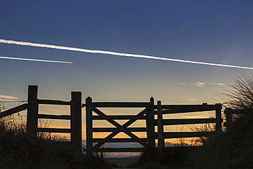 Silhouette Of A Fence At Sunset With Jet Vapour In The Sky, Northumberland, England