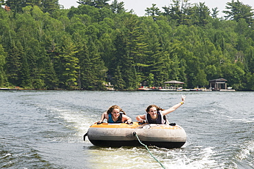 Two Teenage Girls Riding An Inner Tube Being Pulled Behind A Boat In A Lake, Ontario, Canada