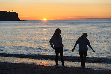 Silhouette Of Two Young Women On A Beach At The Water's Edge At Sunset, Trout River, Newfoundland, Canada