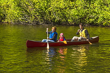 A Couple And Young Girl In A Red Canoe On Byers Lake With Green Forested Shoreline In Byers Lake Campground, Denali State Park, Alaska, United States Of America