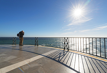 A Man Stands Taking A Photograph At The Railing Along The Water's Edge, Nerja, Malaga, Costa Del Sol, Andalusia, Spain