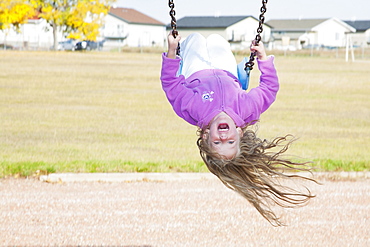 Young Girl On Swing In A Playground In Residential Community On A Cool, Windy Fall Day, Three Hills, Alberta, Canada