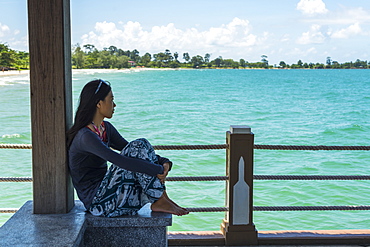 A Young Woman Sits On The Pier At Independence Beach, Sihanoukville, Cambodia