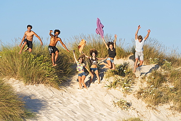 A Group Of Teenagers Running And Jumping Over Sand And Beach Grass, Tarifa, Cadiz, Andalusia, Spain