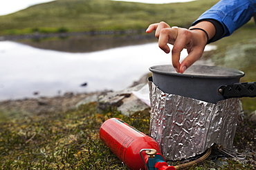 Female Backpacker Cooks With A Backpacker Camp Stove Near The Edge Of A Lake, Alaska