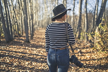 Young Woman Wearing Hat With Camera And Walking Through The Woods Near Creamer's Field, Fairbanks, Interior Alaska, Autumn