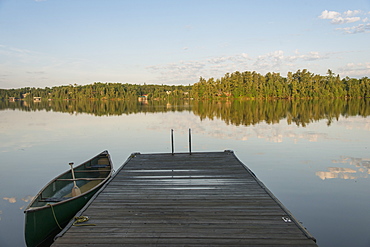 Canoe Beside A Wooden Dock On A Tranquil Lake, Ontario, Canada