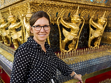 Portrait Of A Woman Standing Beside A Wall With Gold Statues, Temple Of The Emerald Buddha (Wat Phra Kaew), Bangkok, Thailand