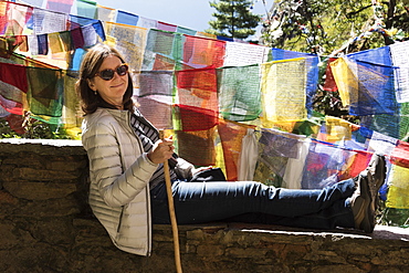 A Woman Rests On A Wall Beside Colourful Prayer Flags, Paro, Bhutan