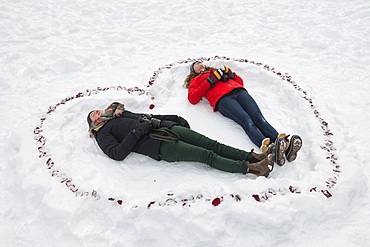 Two Young Women Laying In The Snow Inside A Heart Shape, Alberta, Canada