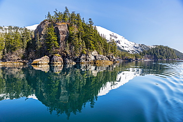 A Tall Outcropping Of Rocks And Evergreen Trees Reflects On The Waters Of Prince William Sound, Whittier, Alaska, United States Of America